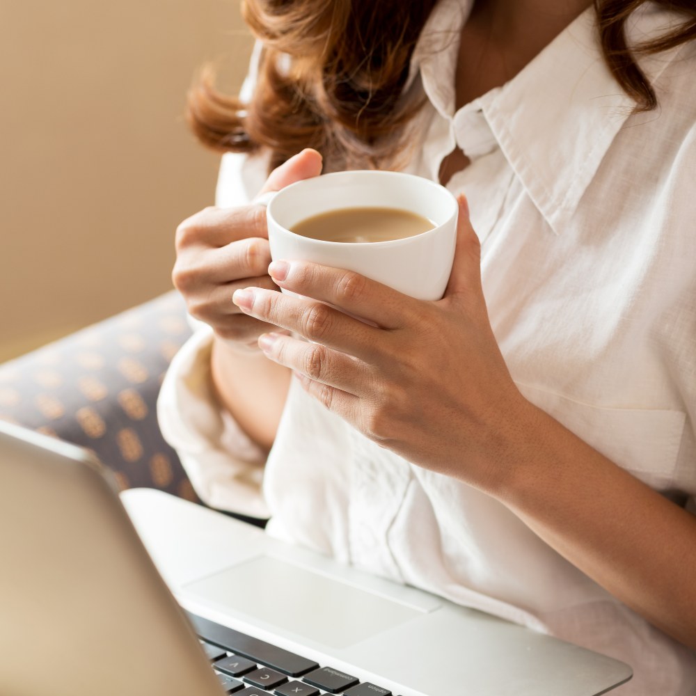 Person holding a cup of coffee in front of a laptop